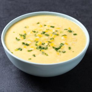 Corn Soup in a white bowl with sprinkled green spring onions on top.