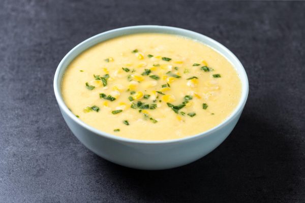 Corn Soup in a white bowl with sprinkled green spring onions on top.